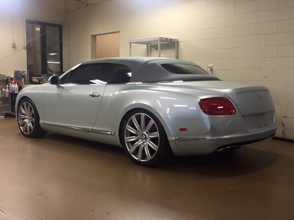 Silver Bentley convertible in a garage, chrome trim, tinted windows, gray top, on a beige floor.