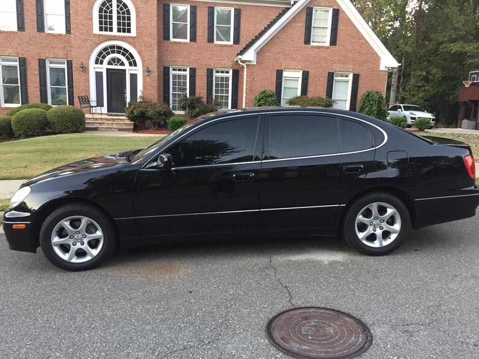 Black Lexus sedan parked on a street in front of a brick house.