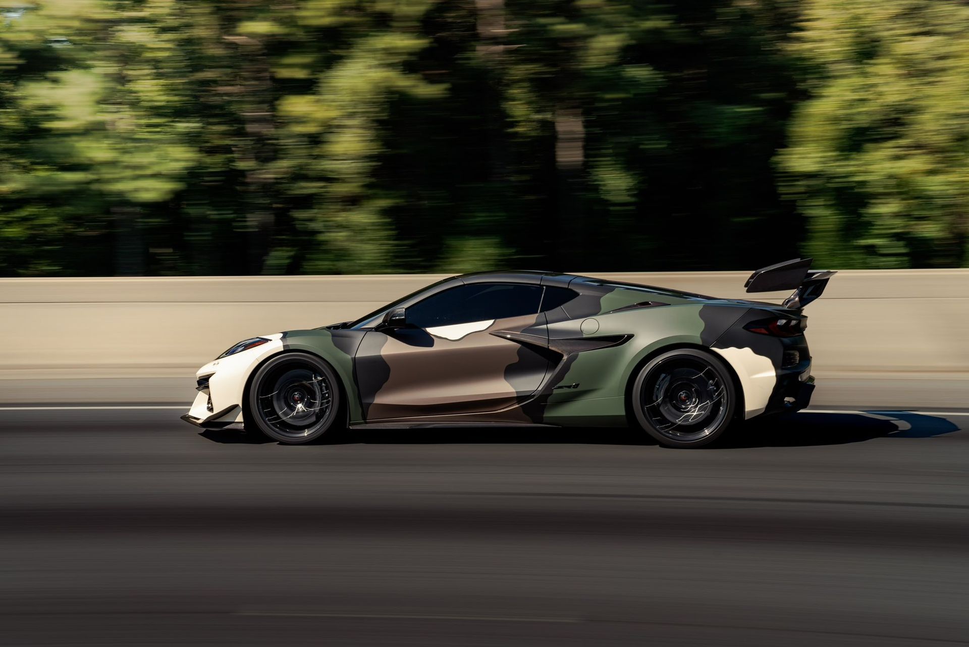 Camouflage-wrapped sports car speeding on a road, trees blurred in the background.