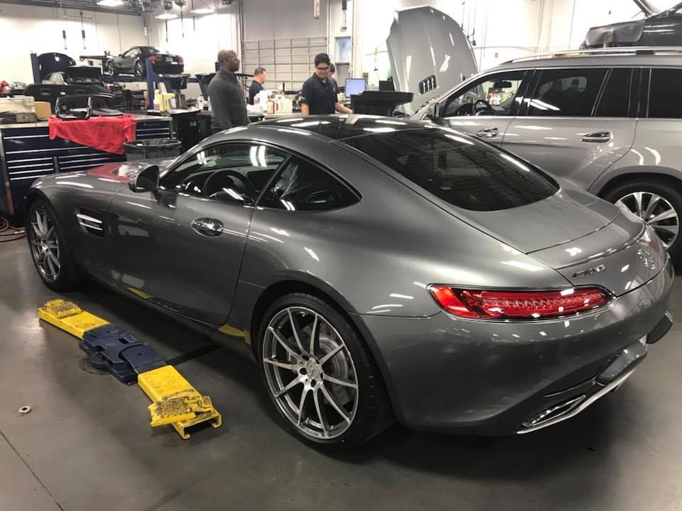 Gray Mercedes-AMG GT sports car in a repair shop, other cars and mechanics visible.