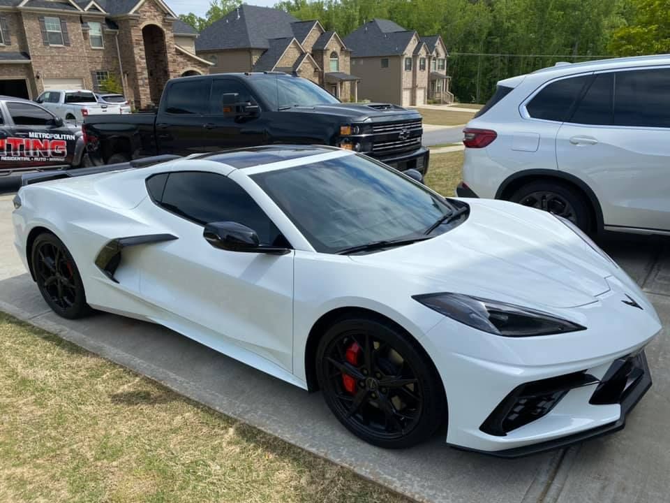 White sports car parked on driveway, black wheels, red brake calipers. Other cars and houses in background.