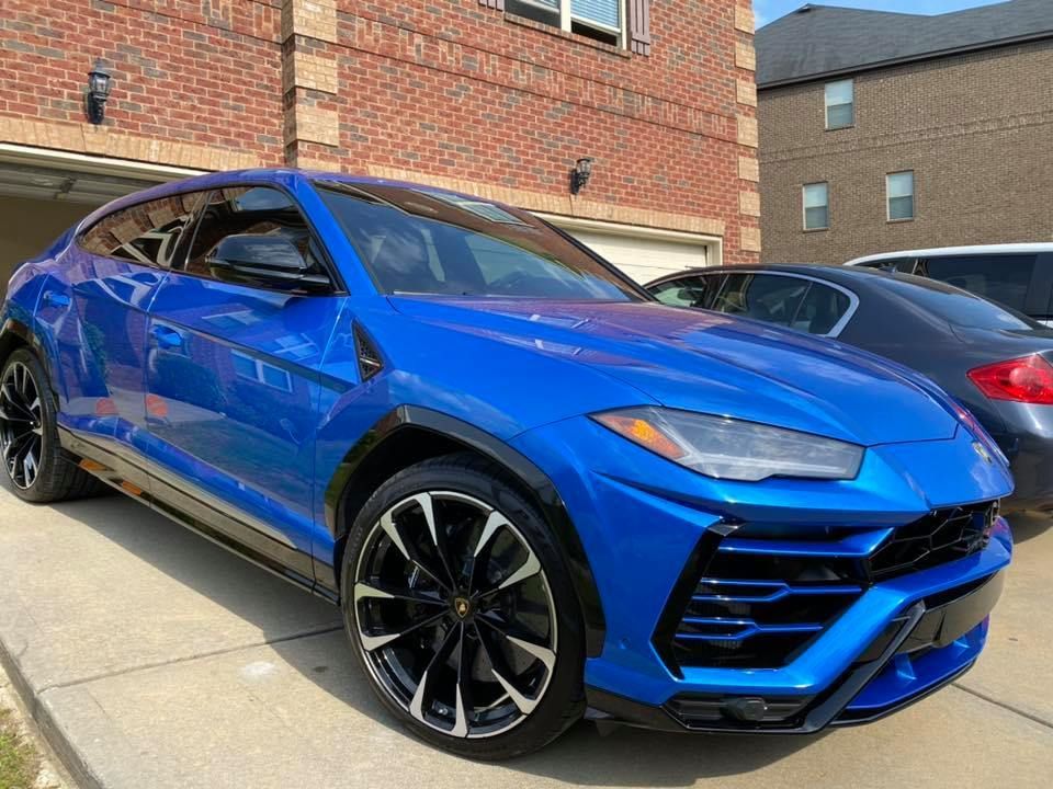 Blue Lamborghini Urus SUV parked in front of a brick house.