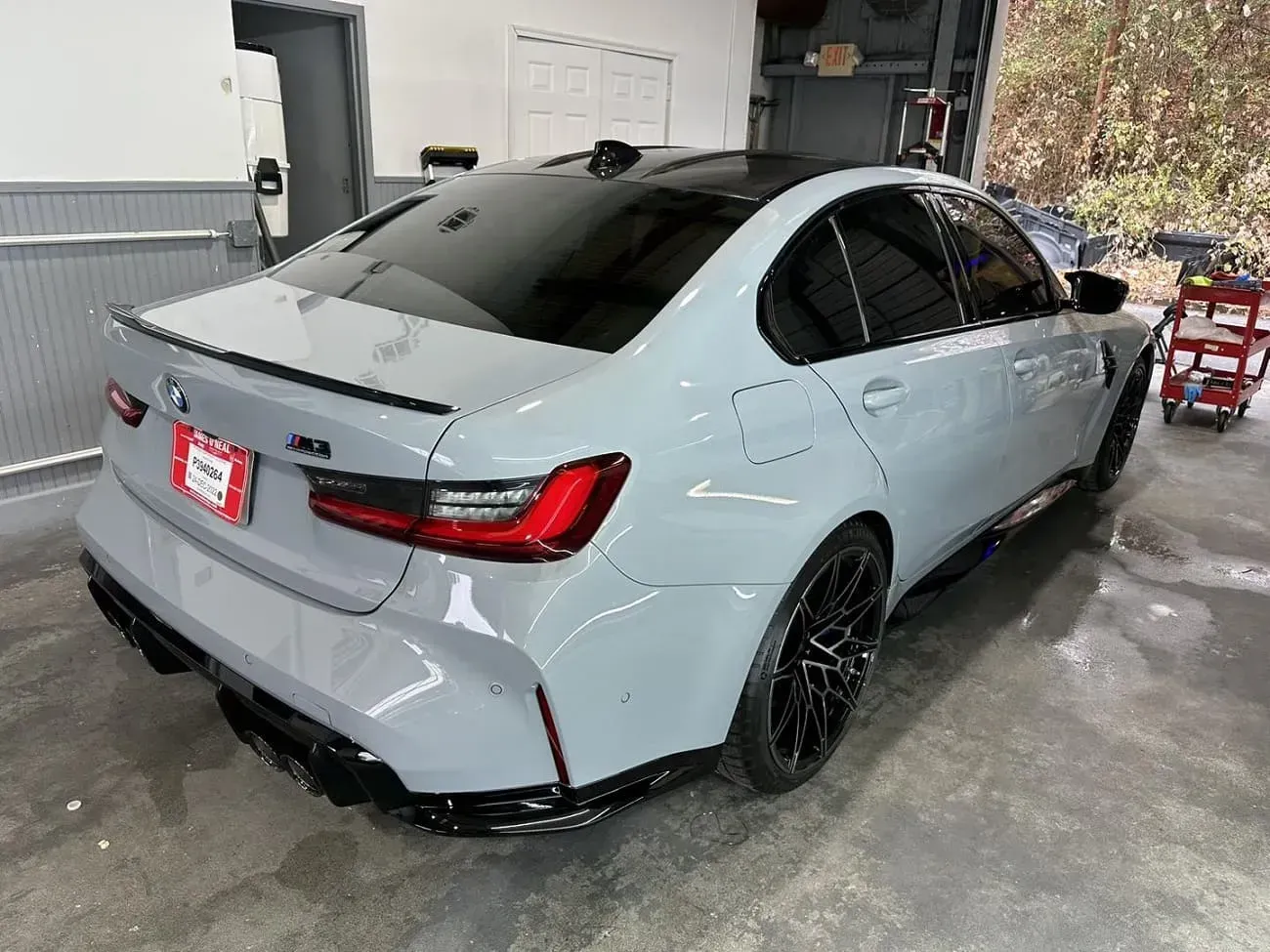 Gray BMW M3 sedan with black accents parked inside a garage, license plate visible.