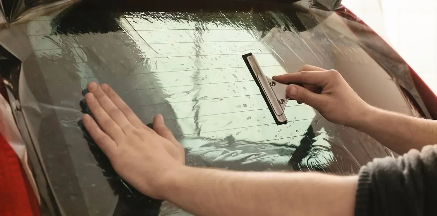 Person applying tint film to a car window with a squeegee.