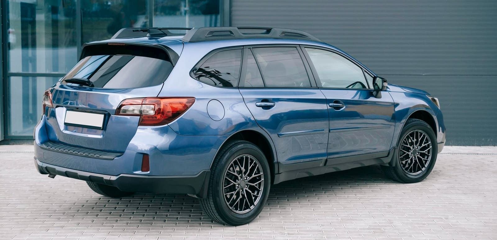 Blue Subaru Outback parked in front of a gray building.