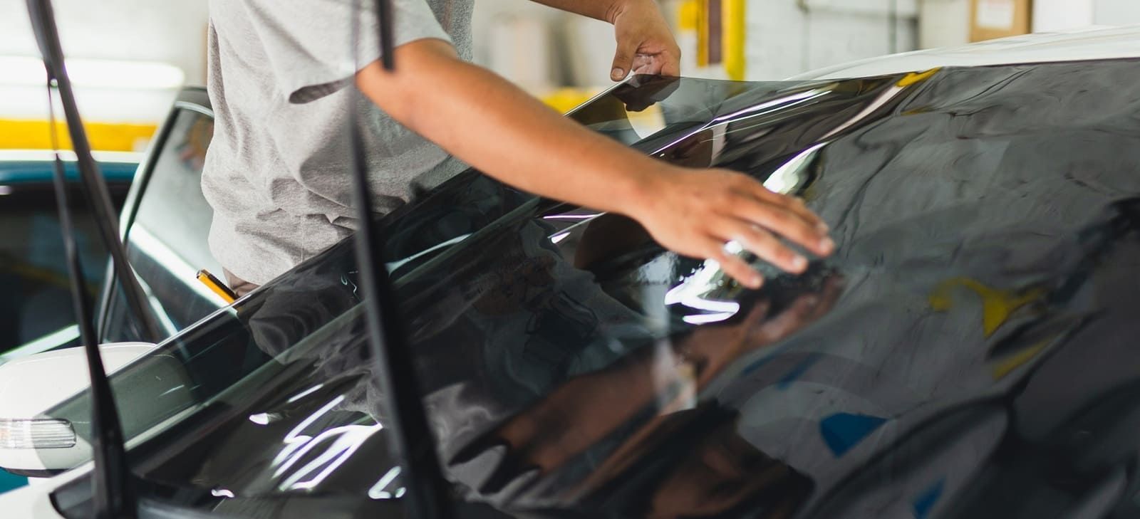 Person applying window tint to a car windshield.