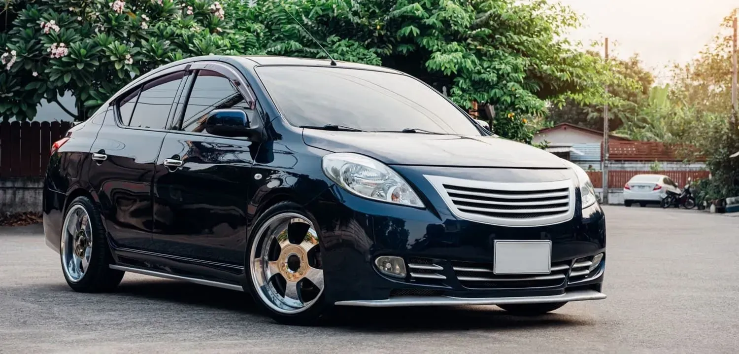 Dark blue sedan car with customized rims parked on a concrete surface with greenery in the background.