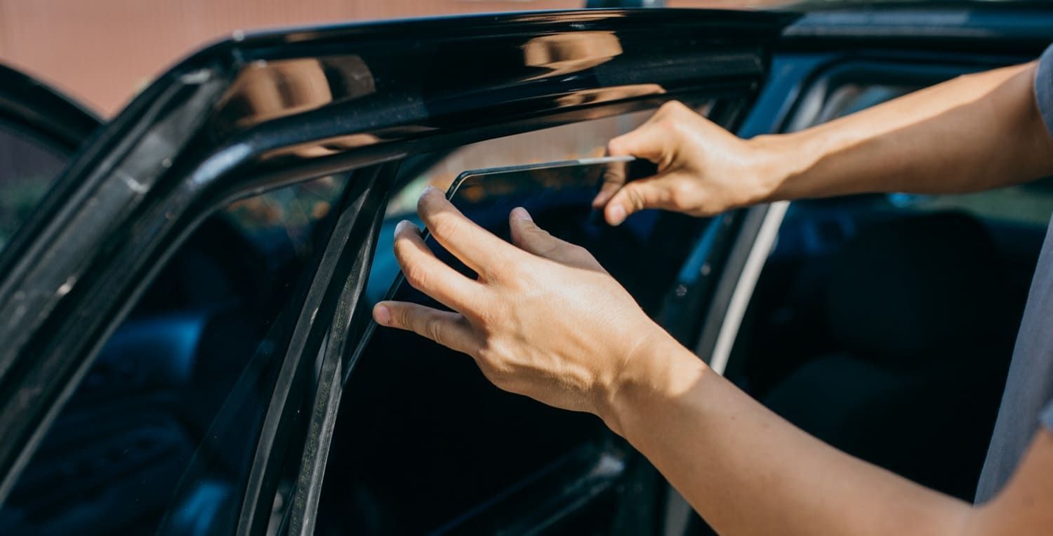Person installing a car window visor. They are holding a tool and adjusting it on a black car door.