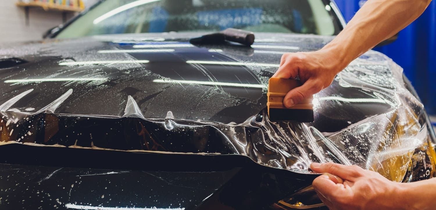 Person applying protective film to a car hood with a squeegee.