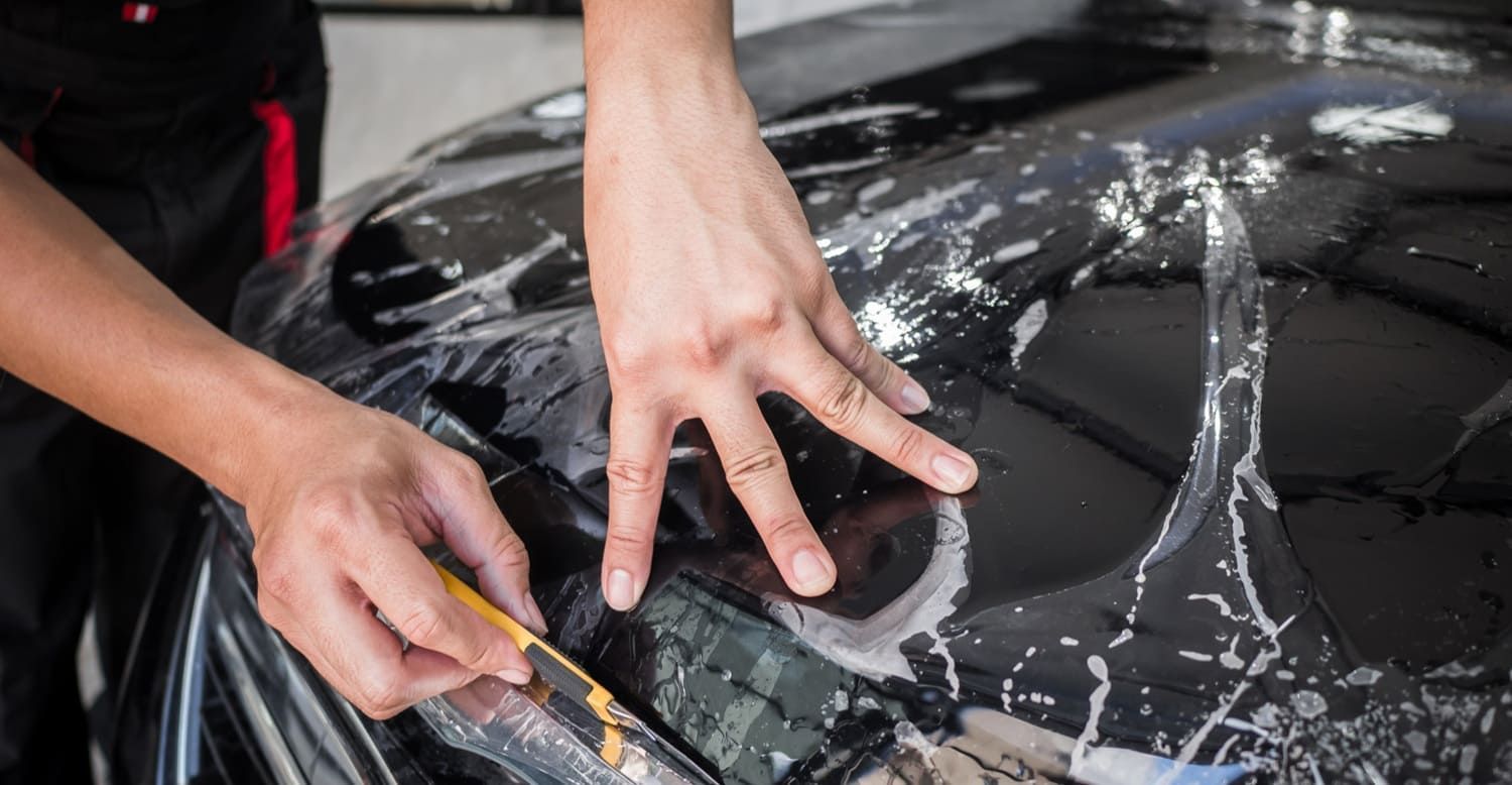 Hands applying film to a car hood with a squeegee, detail of the process.