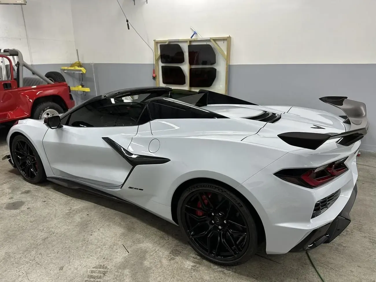White convertible sports car with black wheels and spoiler in a garage.