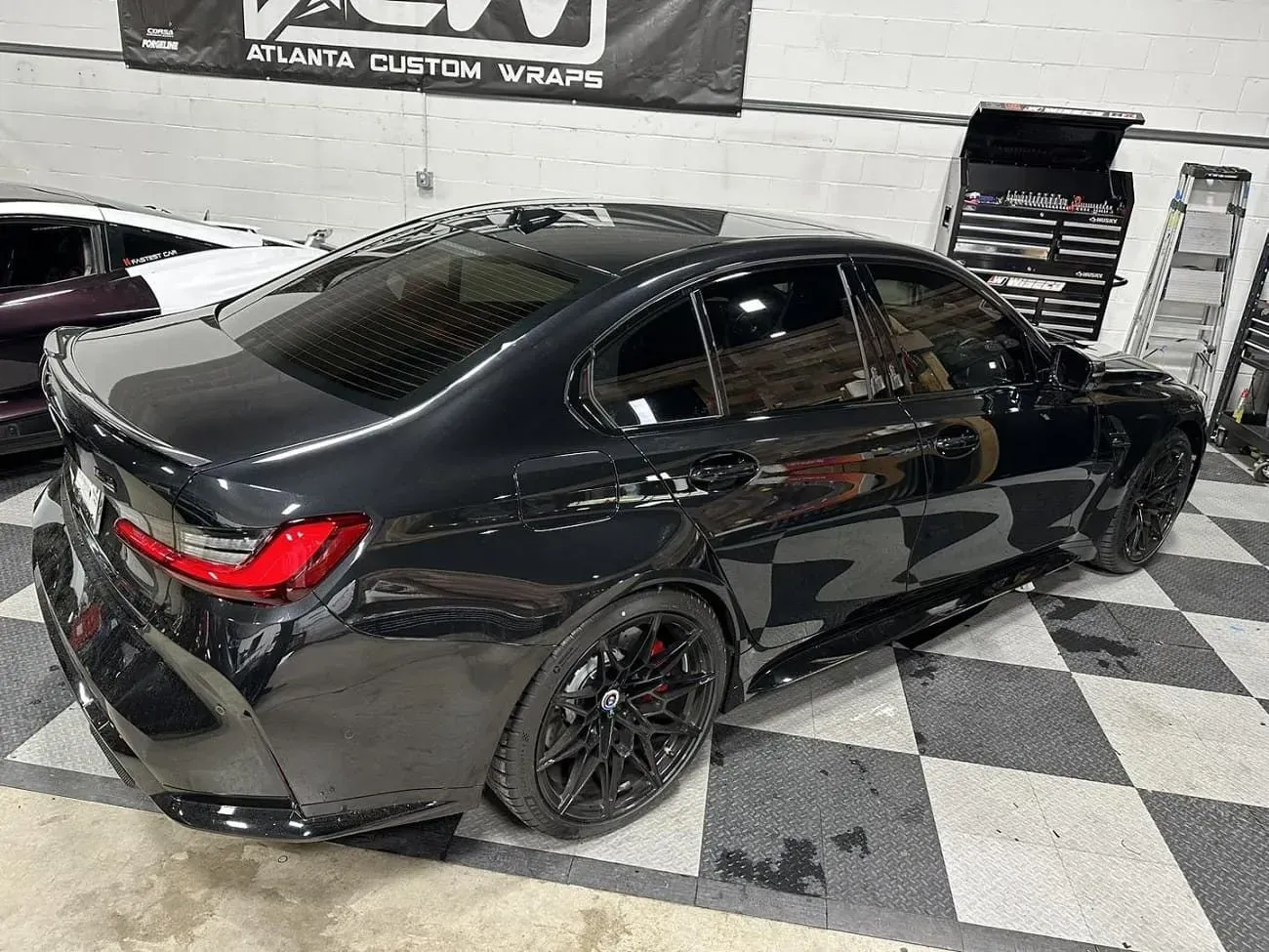 Black sedan in a shop with checkered floor. Tinted windows, black rims, red brake calipers visible.