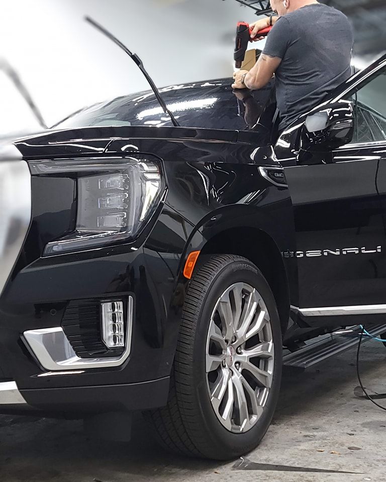 Black GMC Yukon being worked on by a person; applying tint film to windshield.