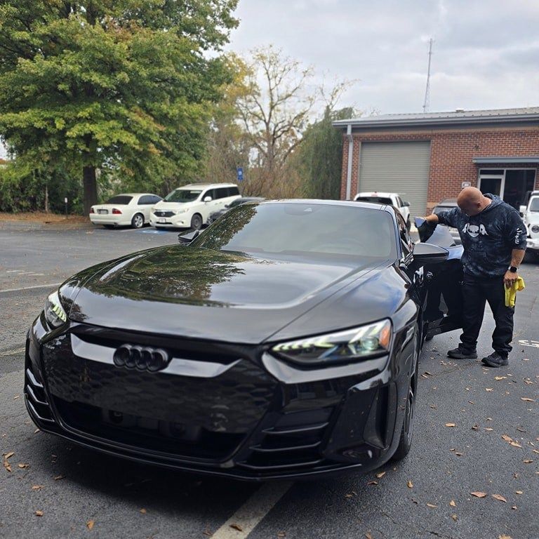 Black Audi being detailed by a person outside a building.