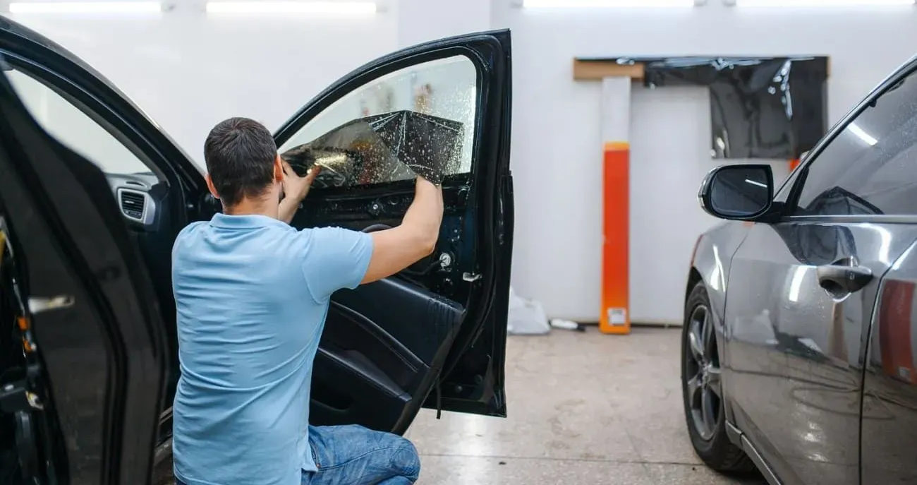 Person applying tint to a car window inside a garage.