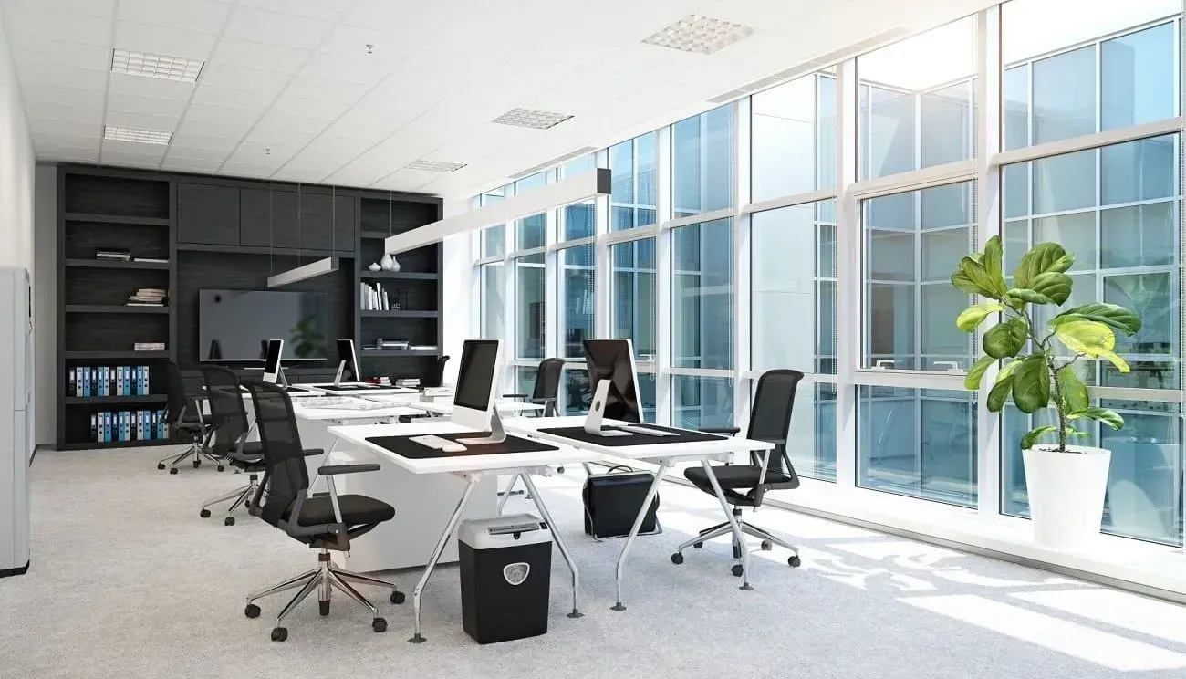 Modern office with desks, computers, chairs, and large windows with natural light.