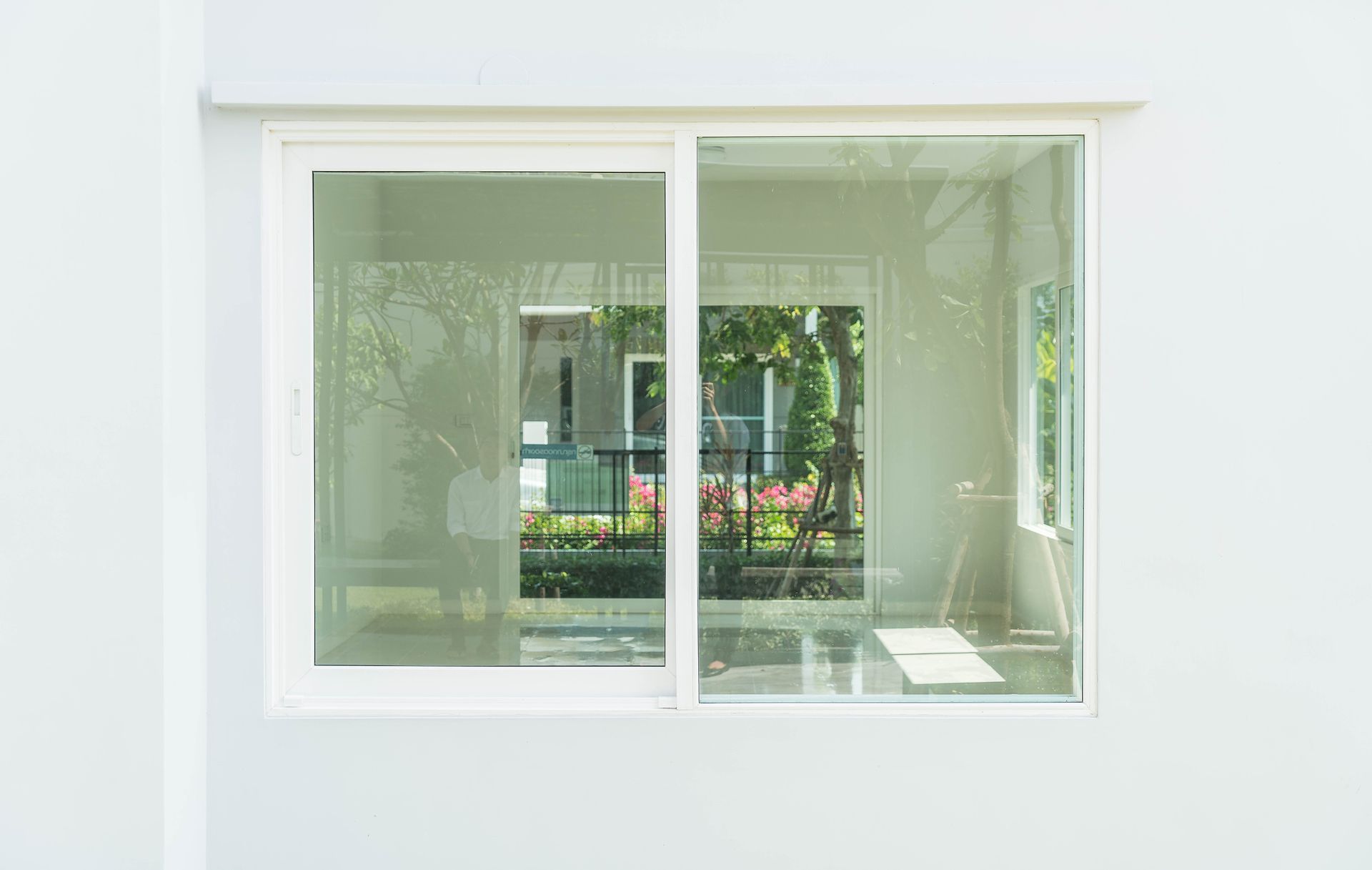 White sliding glass window on a white wall, reflecting an outdoor scene.