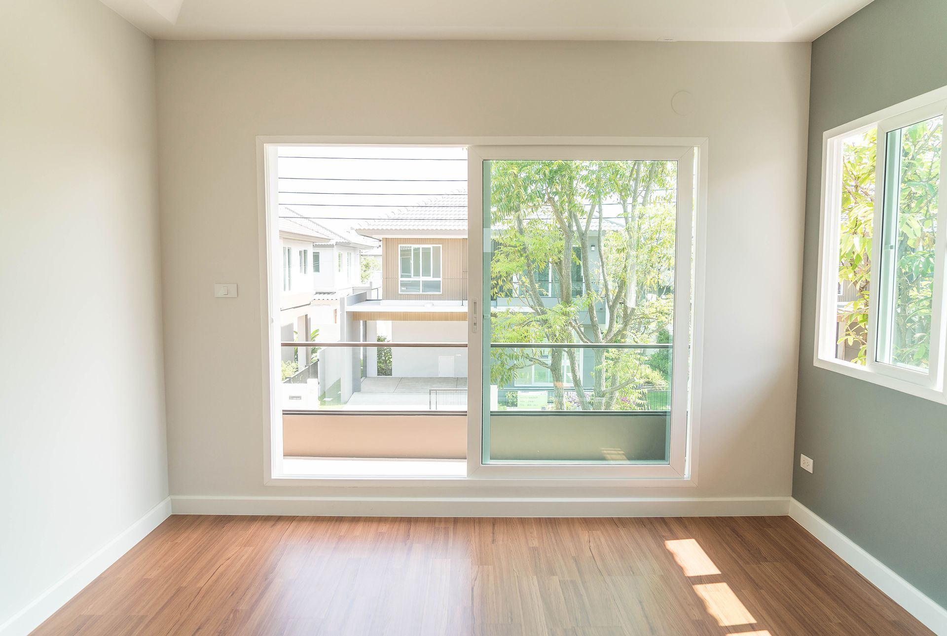 Empty room with a large sliding glass door and a smaller window. Brown wood floor and neutral walls.