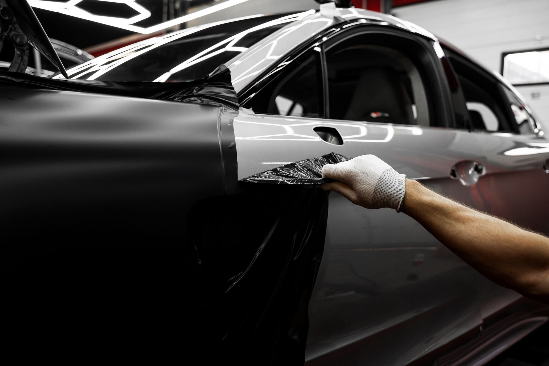 Person peeling black vinyl wrap on a car door, revealing silver paint beneath.