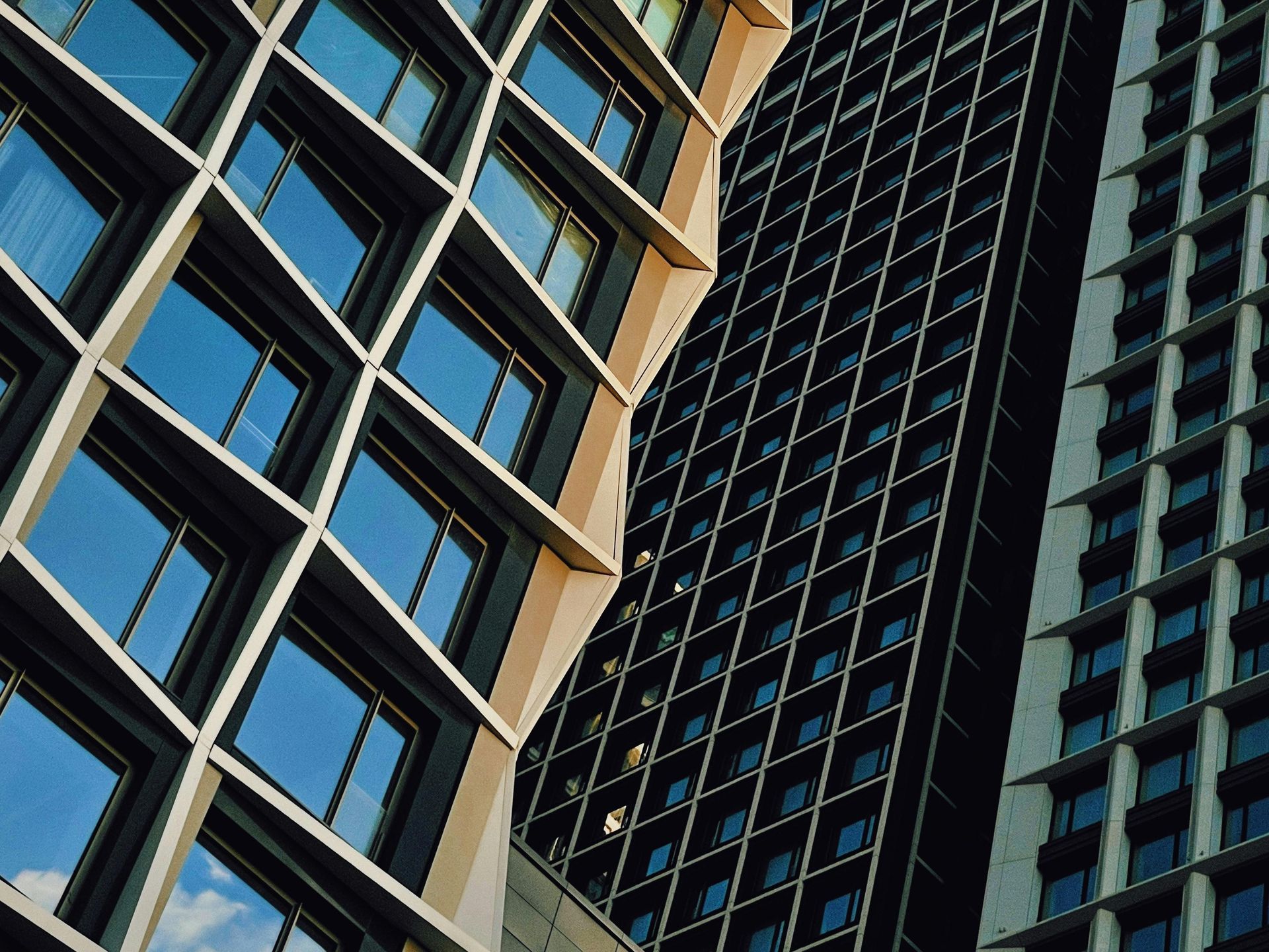Modern buildings with geometric facades, including a diagonal grid and rectangular patterns, against a blue sky.