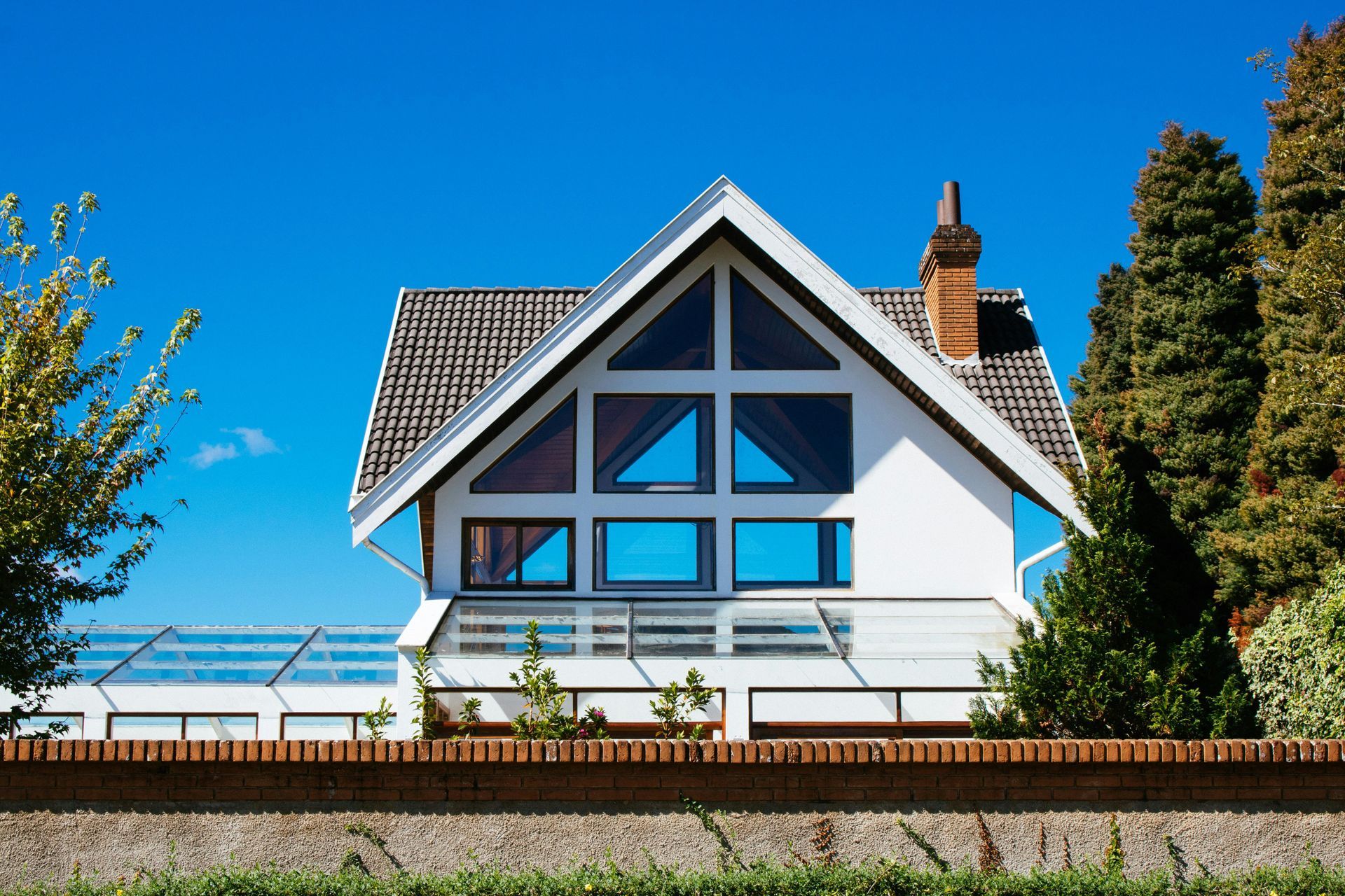 White house with a triangular roof and large windows, against a bright blue sky.