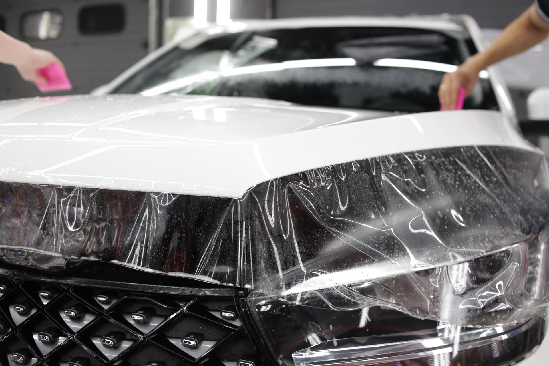 Car being wrapped in protective film by two people, using pink squeegees.