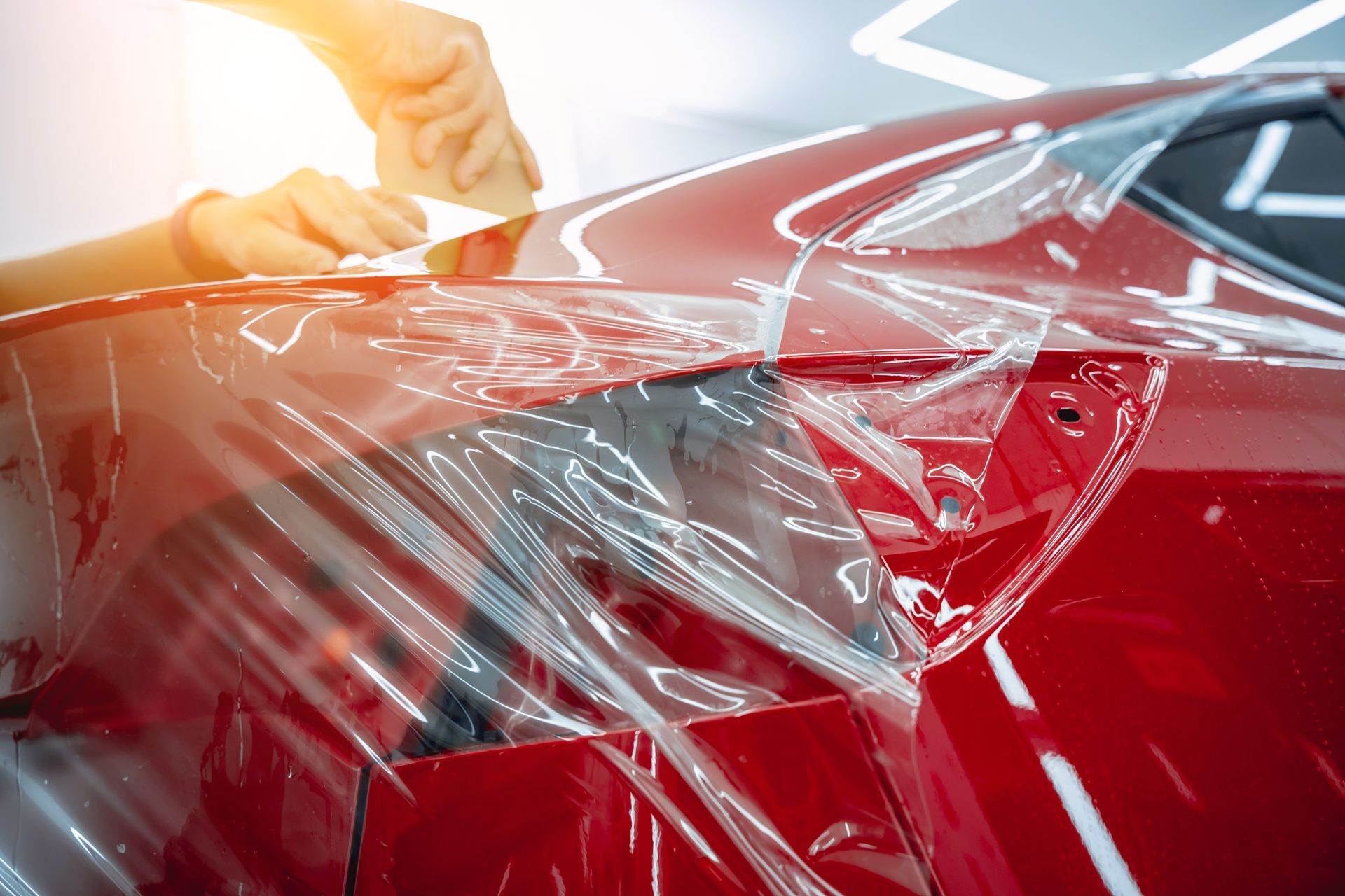 Person applying clear protective film to a red car's body.