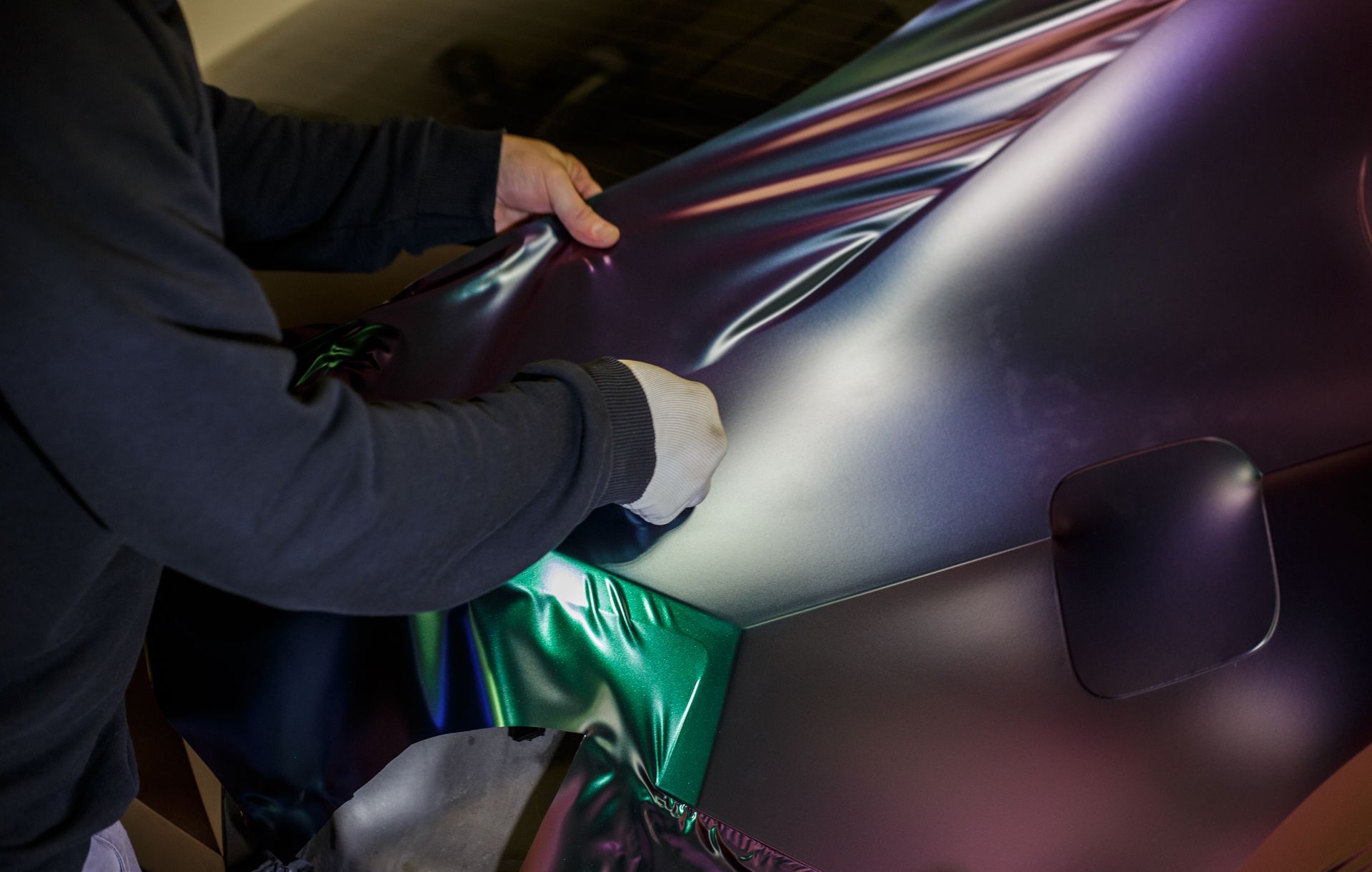 Person installing iridescent vinyl wrap on a car. Hands, tools, and close-up of the body.