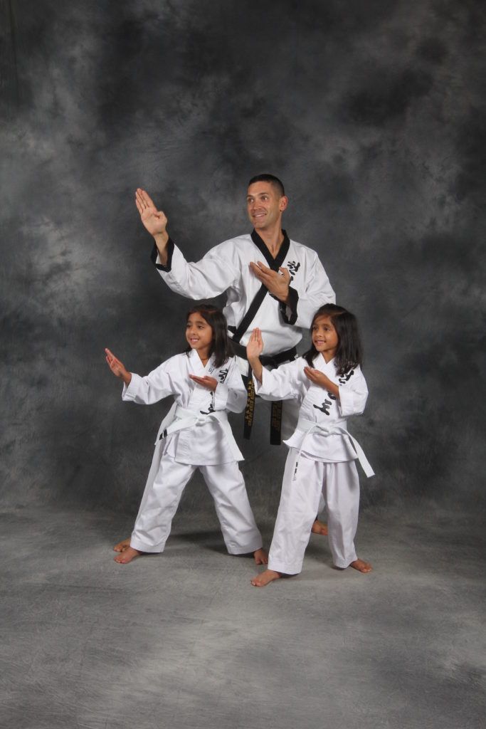 A man and two little girls are practicing martial arts.