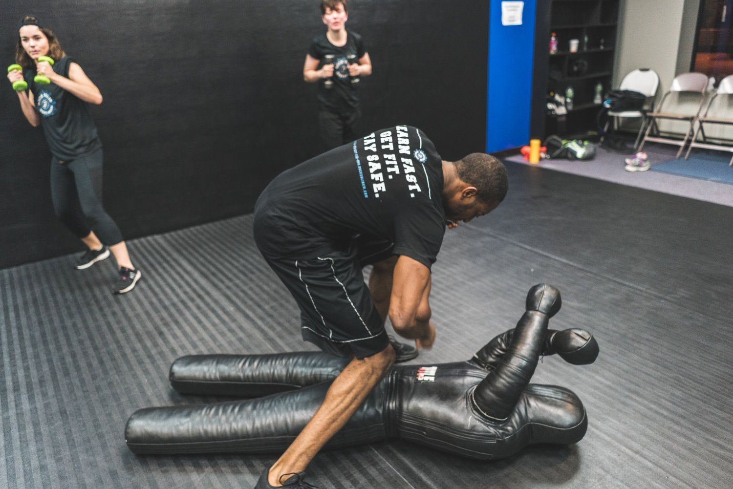 A man is kneeling on a mannequin in a gym.