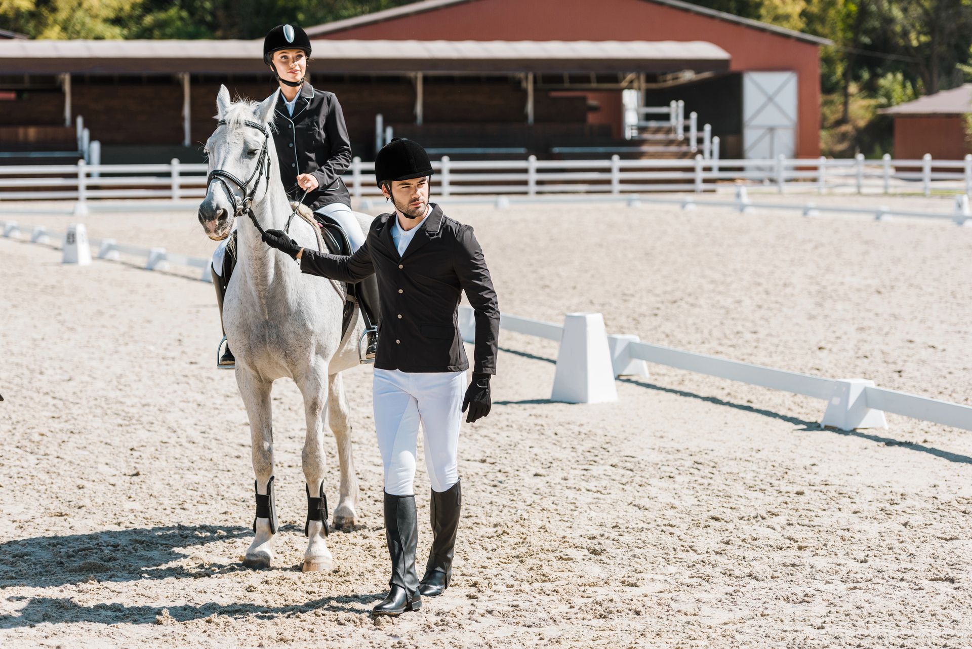 Un uomo allena un cavaliere su un cavallo bianco in un maneggio all'aperto.