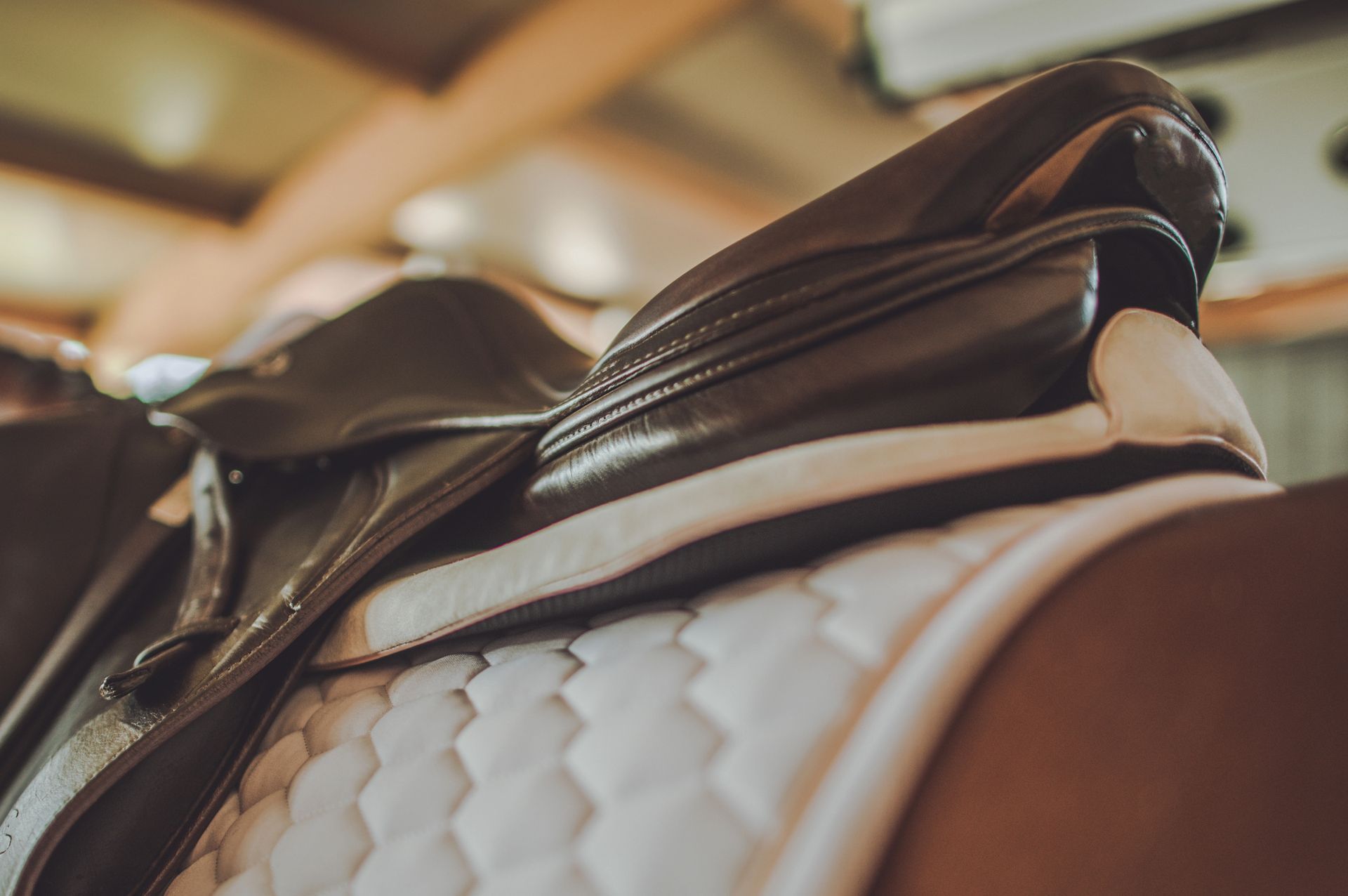 Primo piano di una sella da cavallo in pelle marrone su un cuscinetto trapuntato bianco.