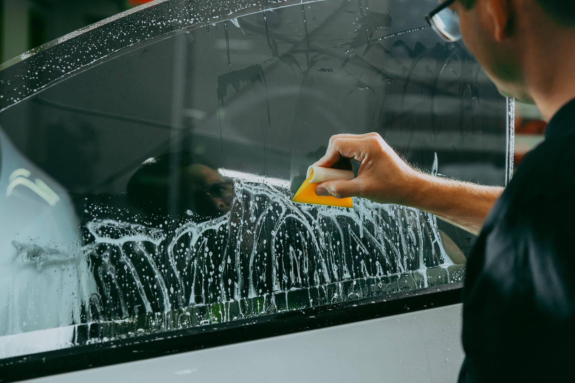 A man is polishing the hood of a car with a polisher.