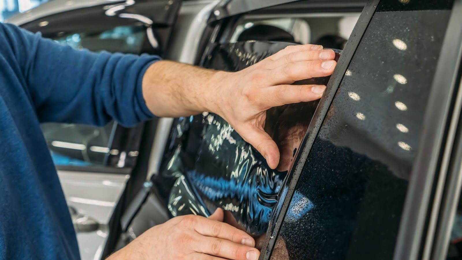 A man is applying tinted glass to a car window.