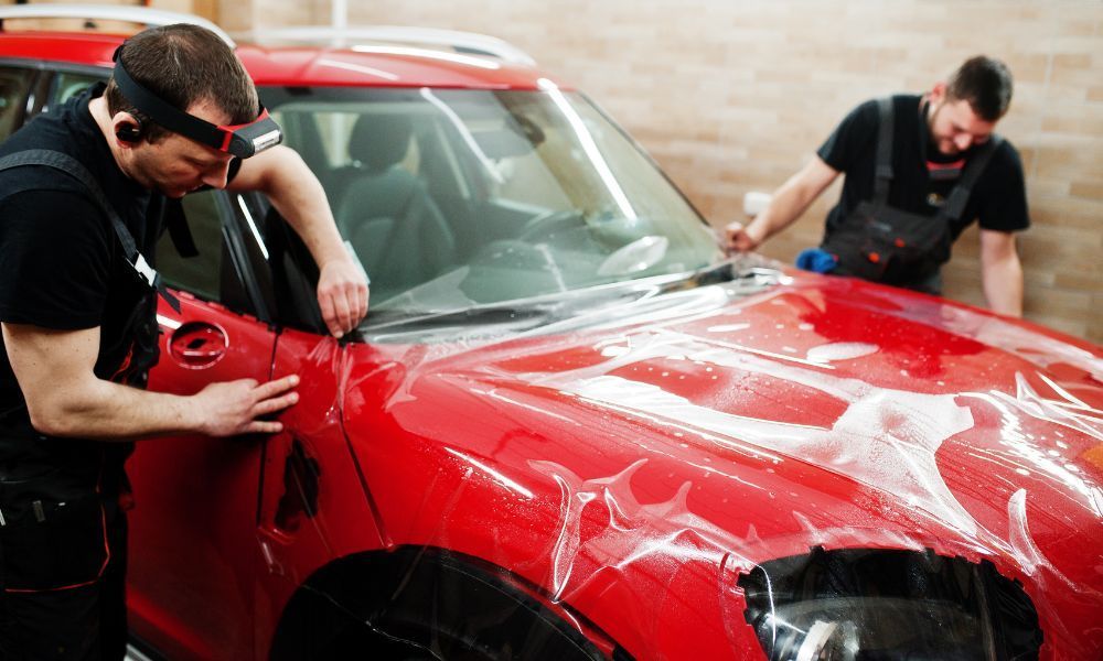 Two men are working on a red car in a garage.