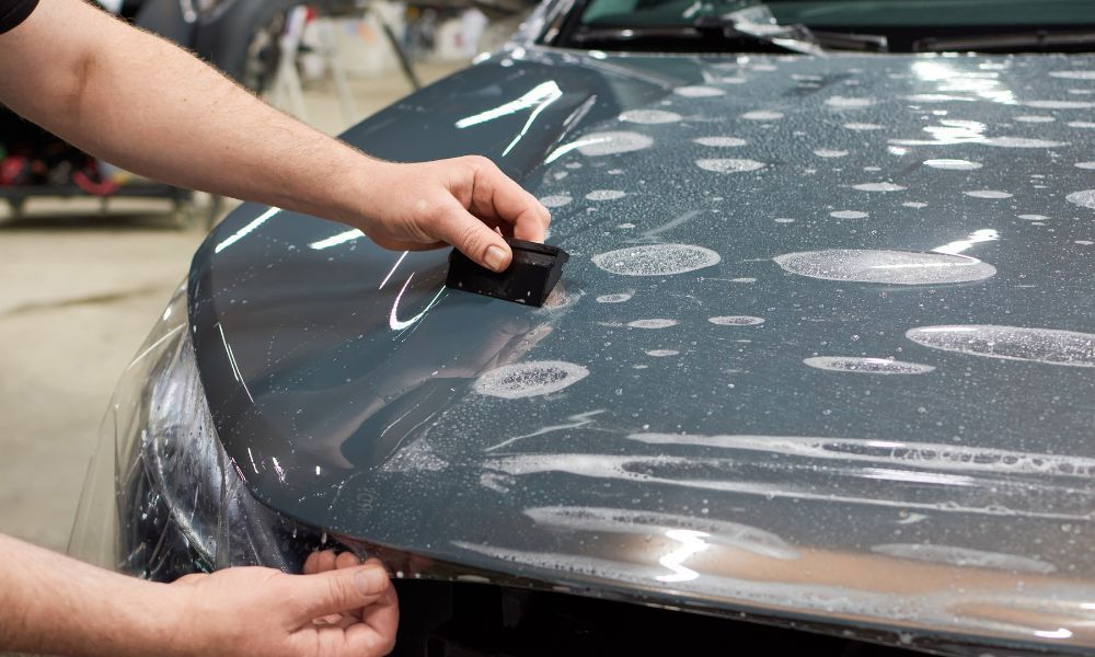 A person is applying a protective film to the hood of a car.