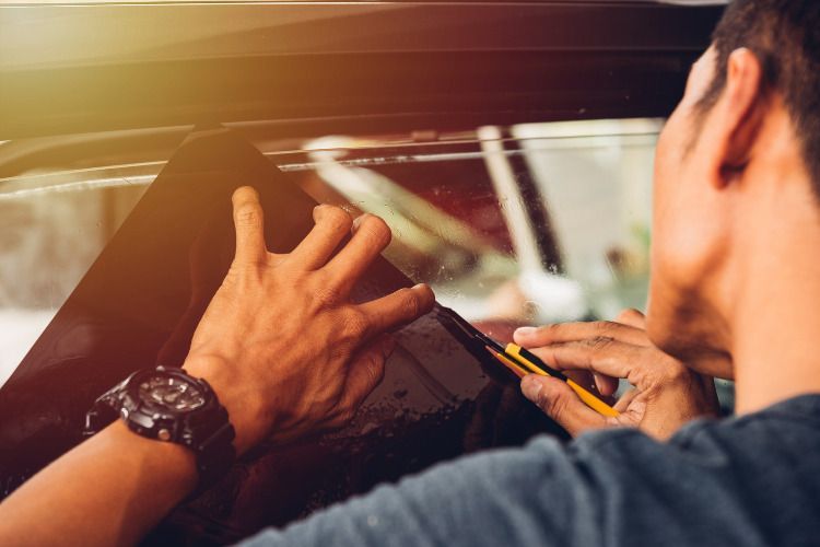 A man is applying tinted glass to a car window.