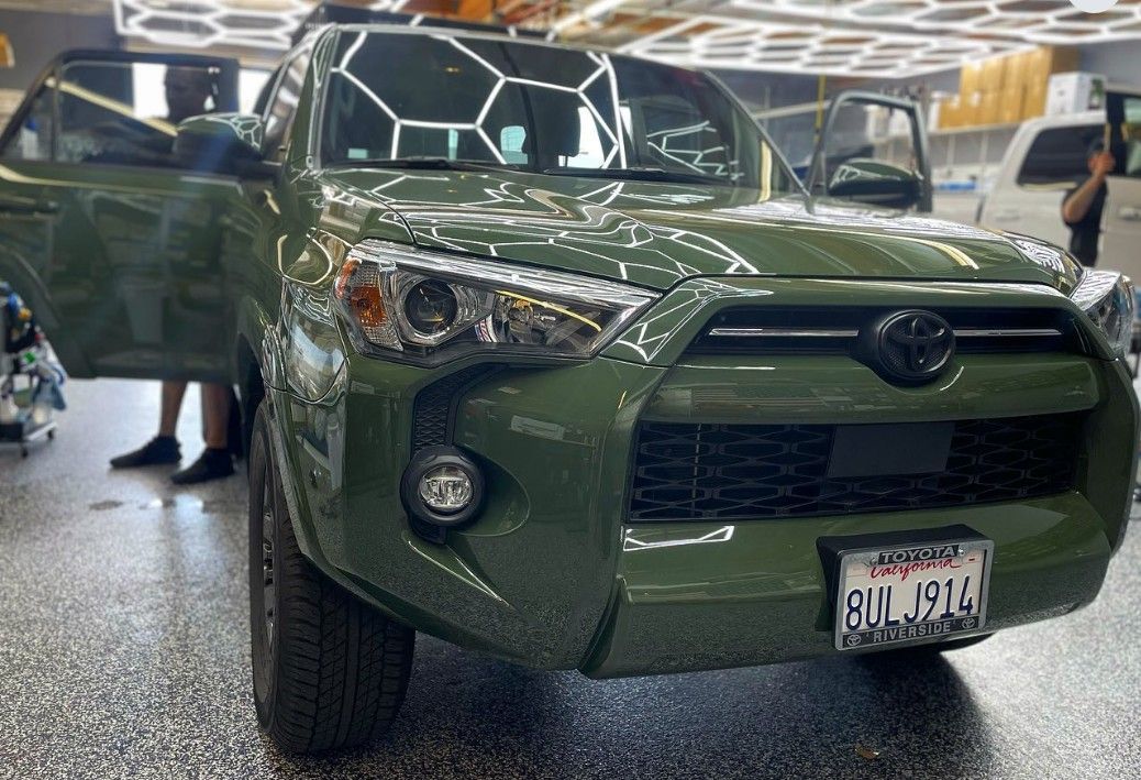 Green Toyota 4Runner with driver's side door open, in a car wash bay.