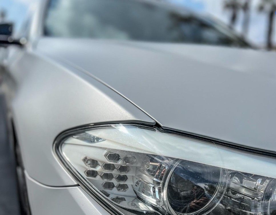 Silver car headlight and hood, close-up with a slightly blurred background.