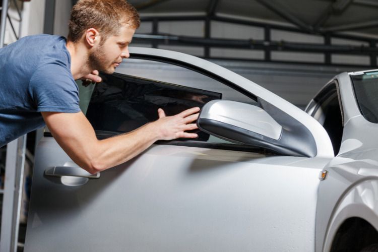 A man is applying tinted window film to a car window.