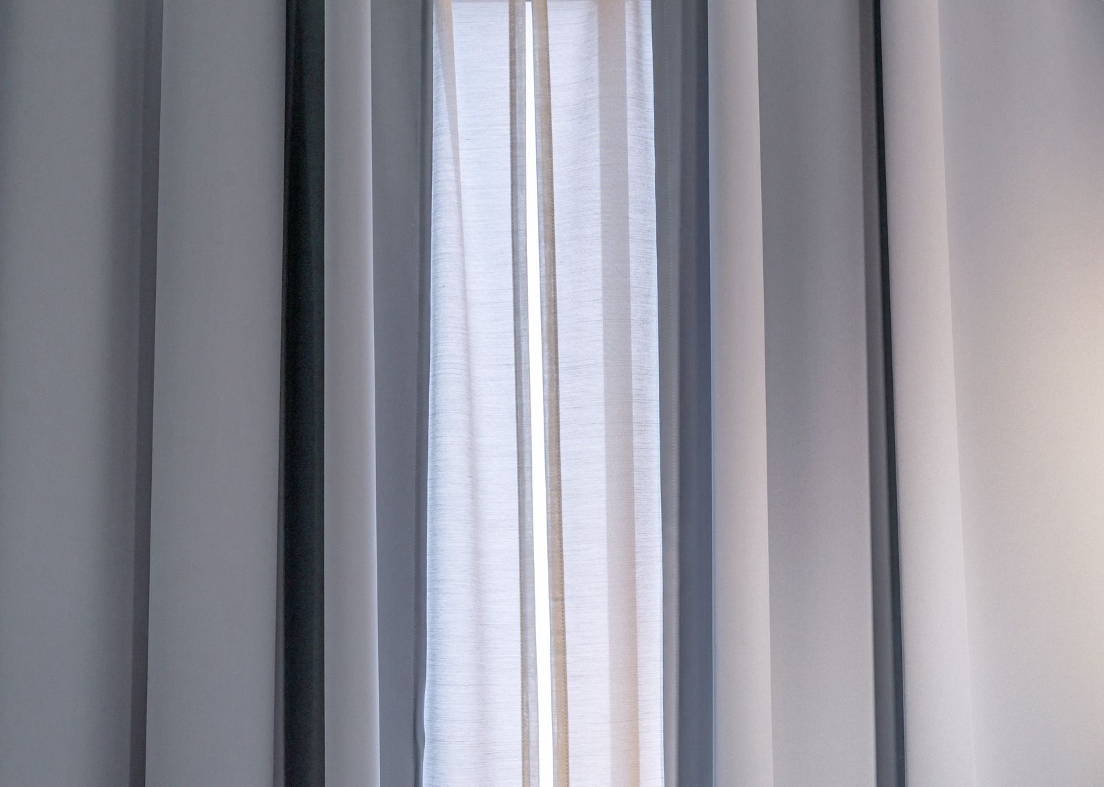 A close up of a window with gray curtains and white sheer curtains.