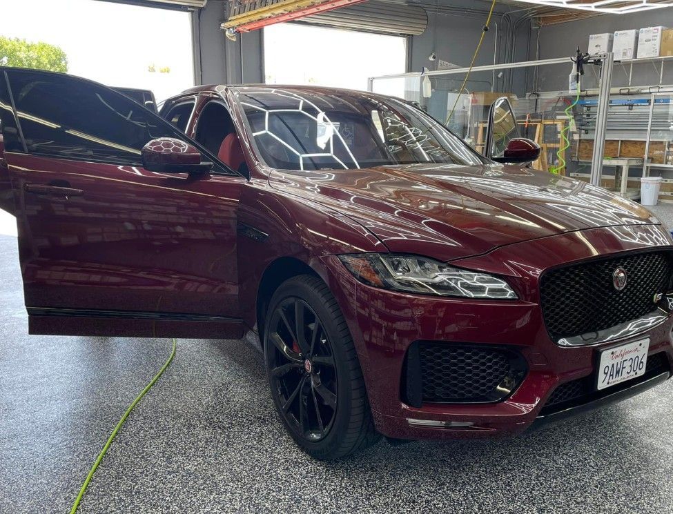Burgundy Jaguar SUV with tinted windows, open driver-side door, parked in a garage.