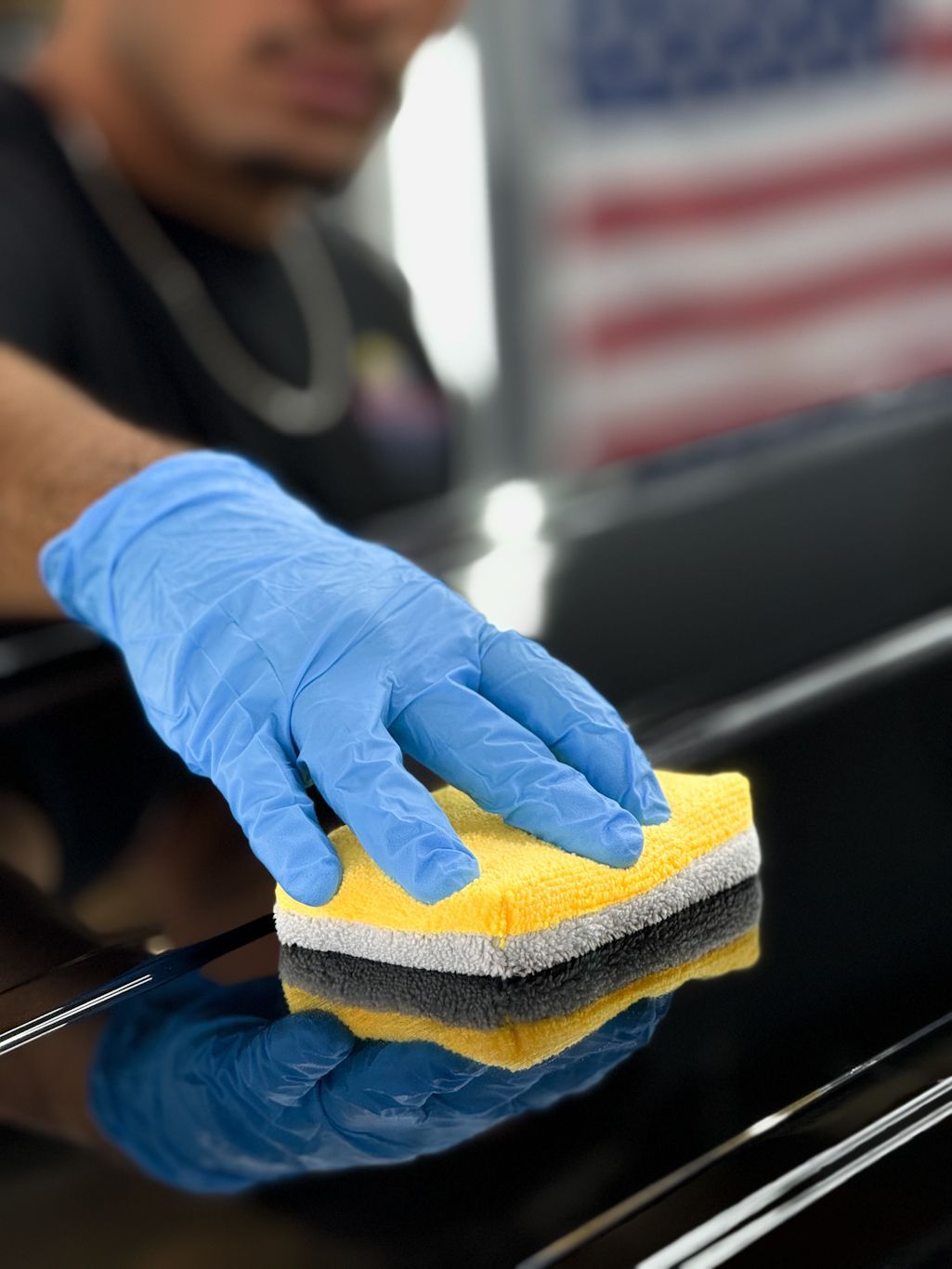 A man wearing blue gloves is cleaning a car with a yellow sponge.