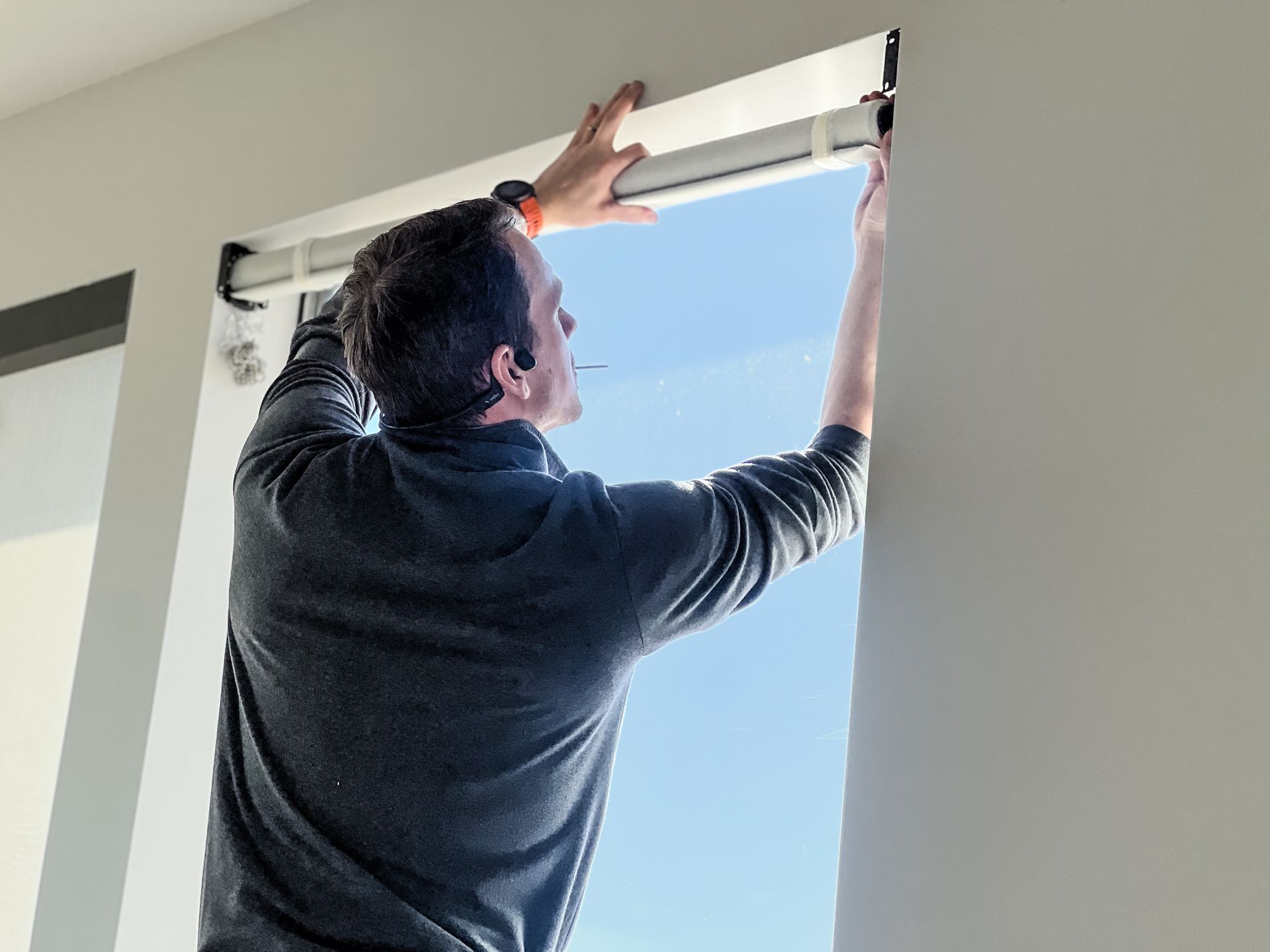 A man is installing blinds on a window.