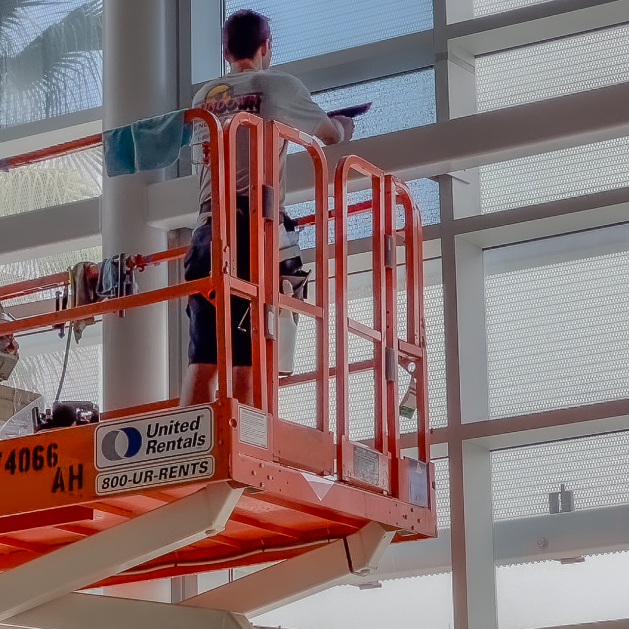 A man is standing on a lift cleaning a window.