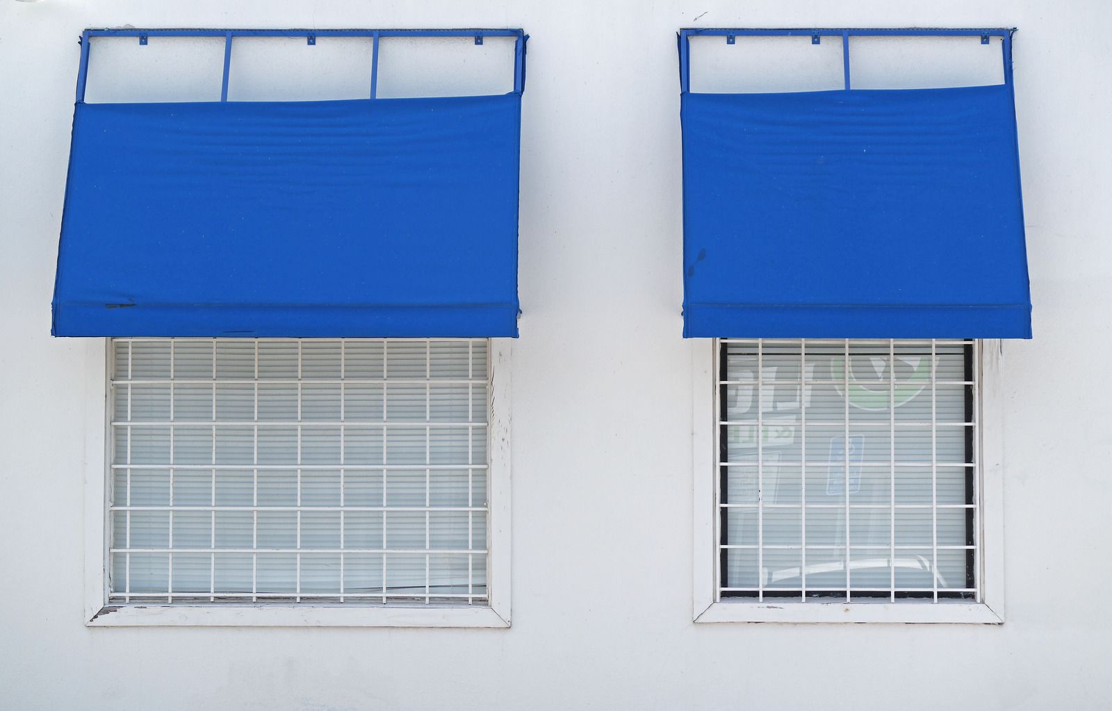 Two windows with blue awnings on them on a white building