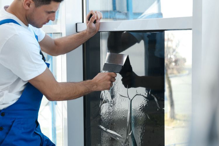 A man is applying tinted glass to a window with a spatula.