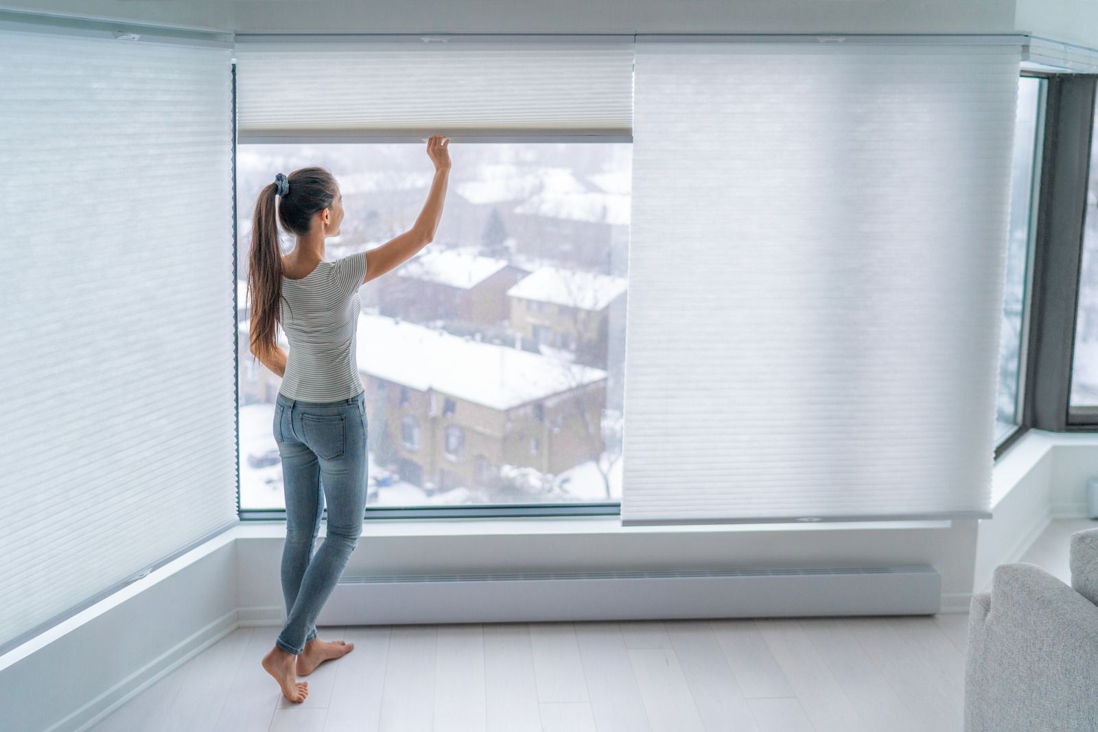 A woman is standing in front of a window looking out.