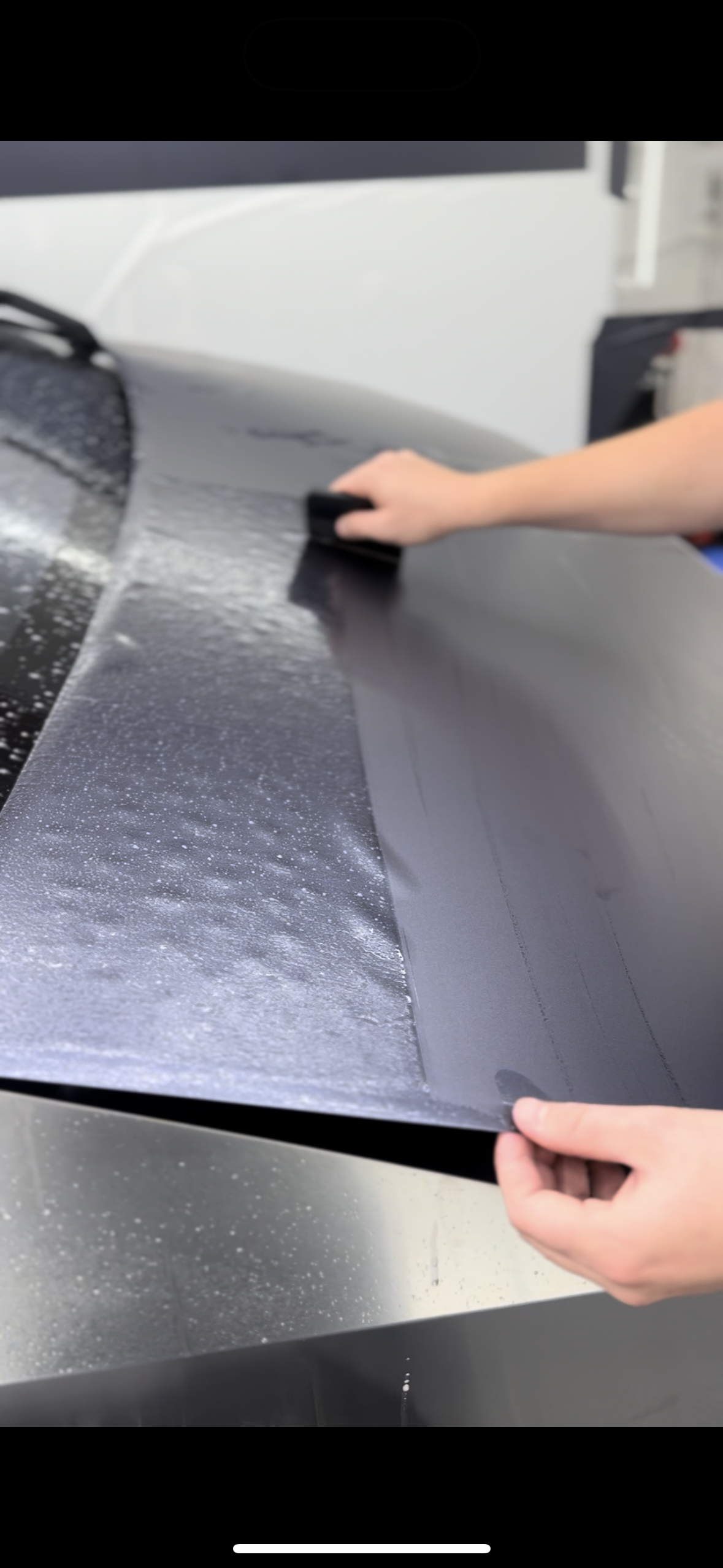 A person is wrapping a car hood with a piece of plastic.