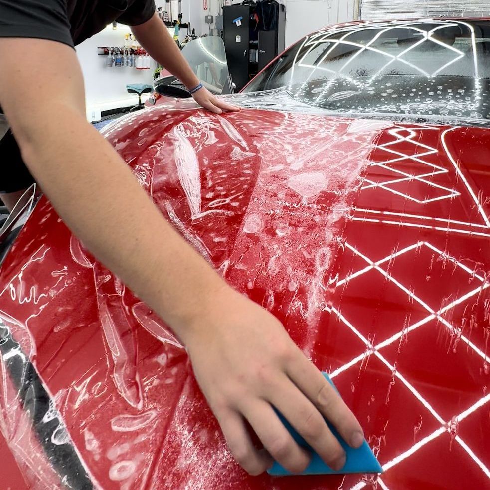 A man is cleaning a red car with a blue sponge